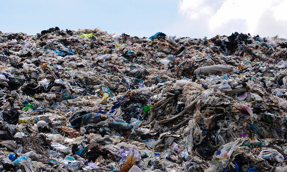 A large pile of plastic waste and trash at a landfill under a cloudy sky.