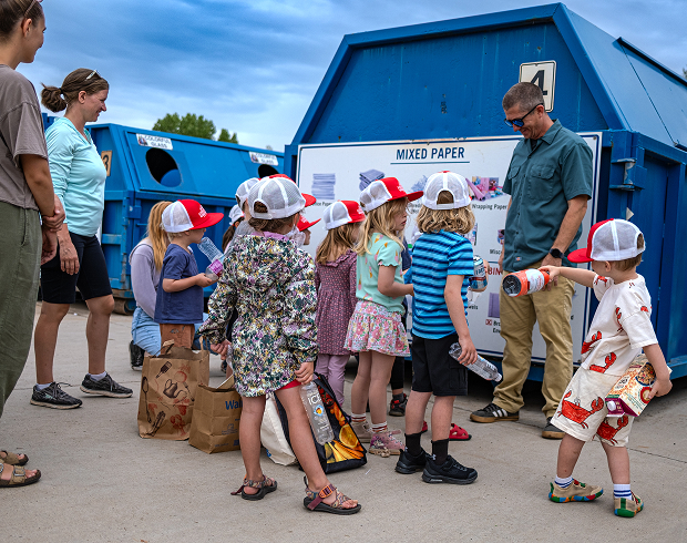 Children and instructors sorting paper and bottles at a community mixed paper recycling dumpster.