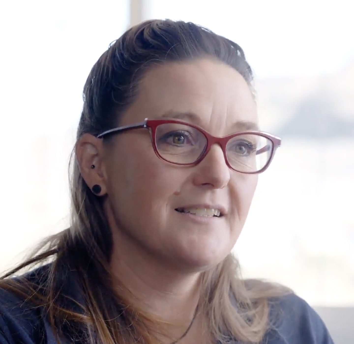 Close-up portrait of a smiling woman wearing red eyeglasses.
