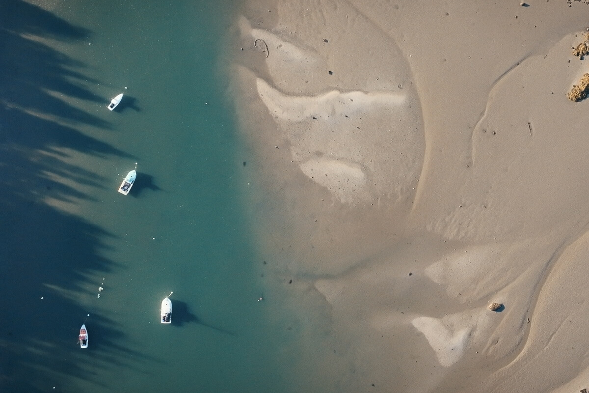 Boats on clear water near sandy shore, showcasing nature and the need to address plastic waste.